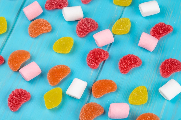 Top view of colorful tasty marmalade candies and marshmallows scattered on blue