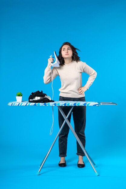 Top view of concerned young girl standing behind the board and holding iron on blue wave surface