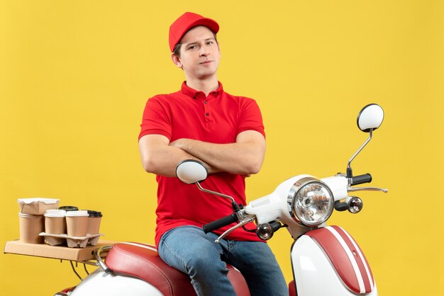 黄色の背景に注文を配信する赤いブラウスと帽子を身に着けている自信を持って野心的な若い男の上面図
