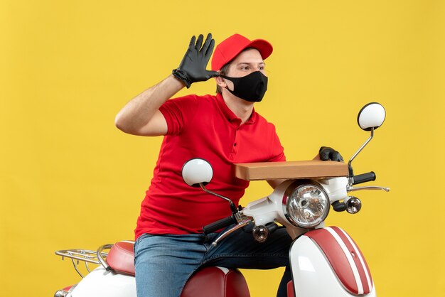 Top view of confident courier man wearing red blouse and hat gloves in medical mask sitting on scooter showing order