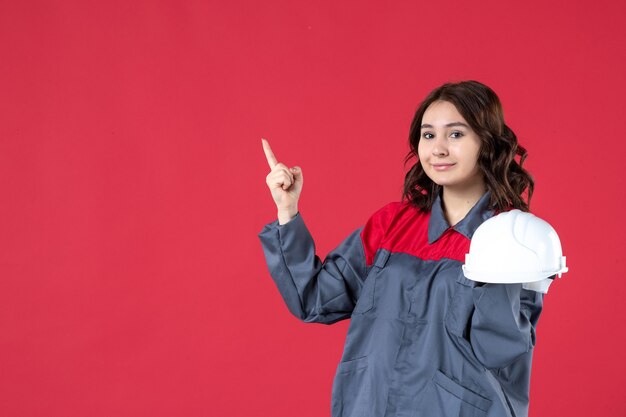 Top view of confident female architect holding hard hat and pointing up on isolated red background