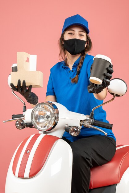 Top view of confident female courier wearing black medical mask and gloves delivering orders on peach background