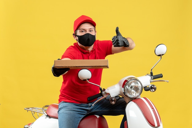 Free photo top view of confident happy courier man wearing red blouse and hat gloves in medical mask sitting on scooter showing order with thumbs up