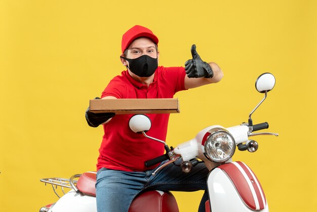 親指を上にして順序を示すスクーターに座っている医療マスクで赤いブラウスと帽子の手袋を着用して自信を持って幸せな宅配便の男の上面図