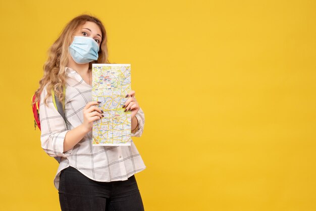 Top view of confident travelling girl wearing her mask and backpack looking at map on yellow 