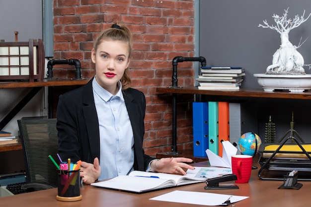 Free photo top view of confident young female sitting at a table and posing for camera in the office