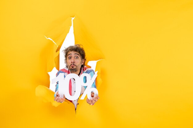 Top view of confused bearded man showing ten percentage in a torn hole in yellow paper