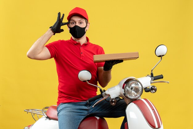 Top view of confused courier man wearing red blouse and hat gloves in medical mask sitting on scooter showing order