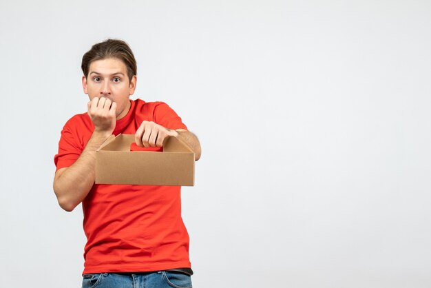 Top view of confused and emotional young man in red blouse holding box on white background