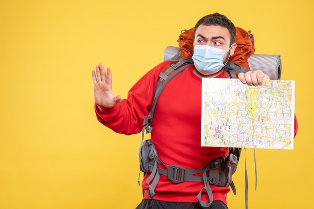 黄色の背景に5つを示す地図を持ったバックパックで医療マスクを着た混乱した旅行者の男性のトップビュー