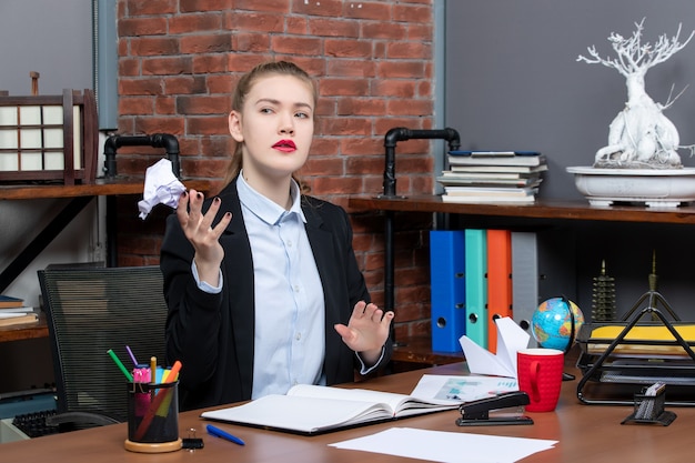 Top view of confused woman sitting at a table and holding wrapped paper in the office