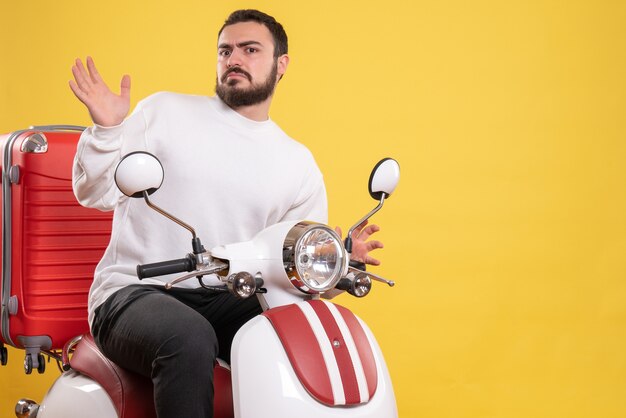 Top view of confused young guy sitting on motorcycle with suitcase on it on isolated yellow background