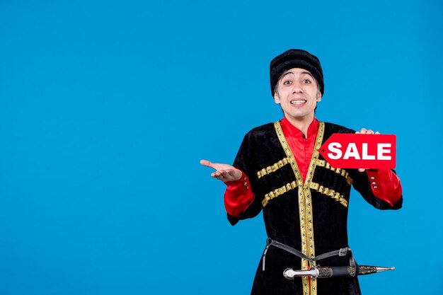 Top view of confused young man in traditional dress showing sale icon on blue wave background