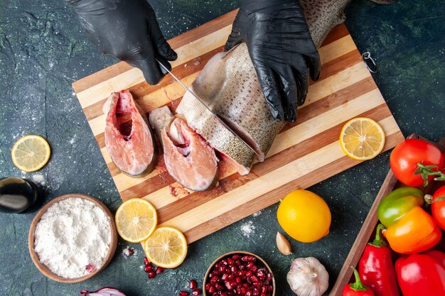 Top view cook cutting raw fish on cutting board flour bowl pomegranate seeds on table