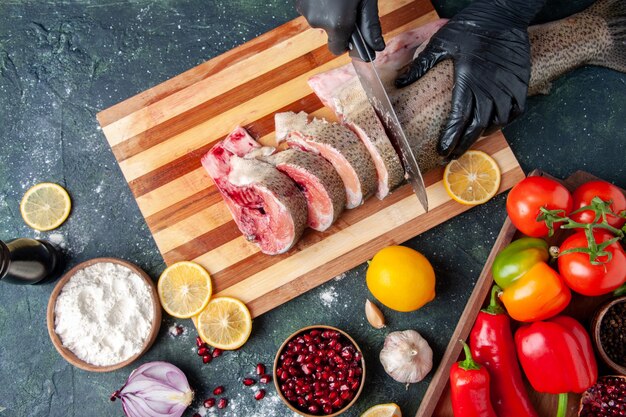 top view cook cutting raw fish on cutting board vegetables on wood board lemon on table