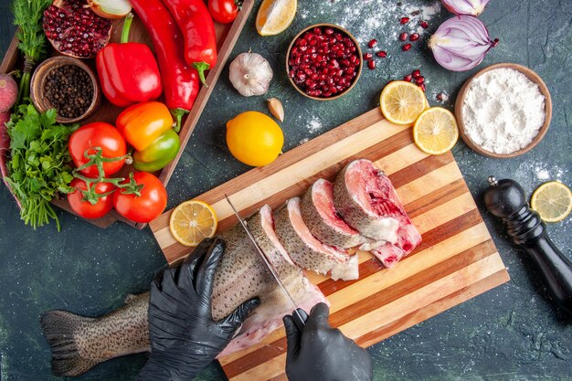 Top view cook cutting raw fish on cutting board vegetables on wood board pepper grinder on table