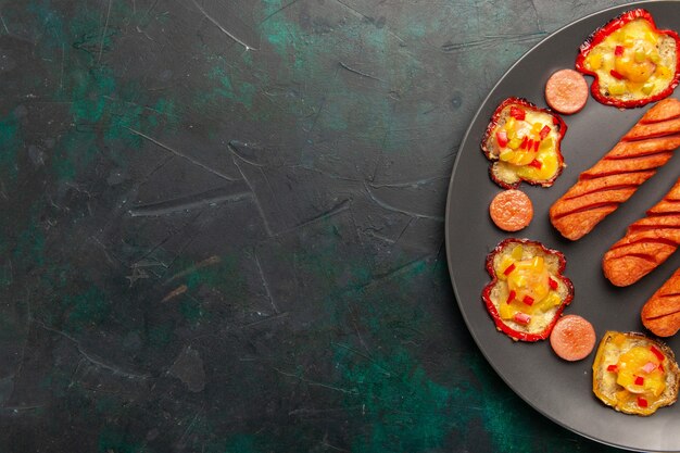 Top view cooked bell-peppers with fried sausages inside plate on dark green desk