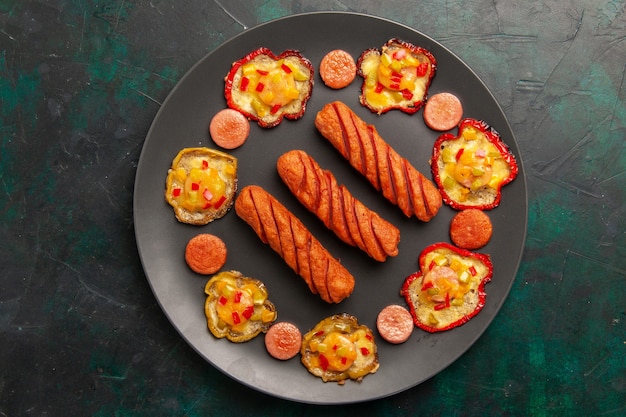 Top view cooked bell-peppers with fried sausages inside plate on dark-green surface