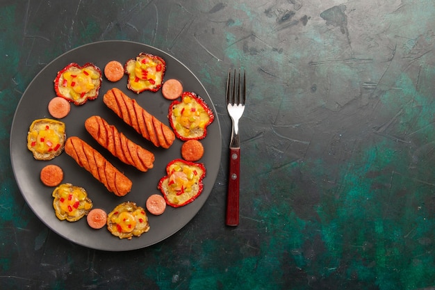 Top view cooked bell-peppers with sausages on dark-green desk