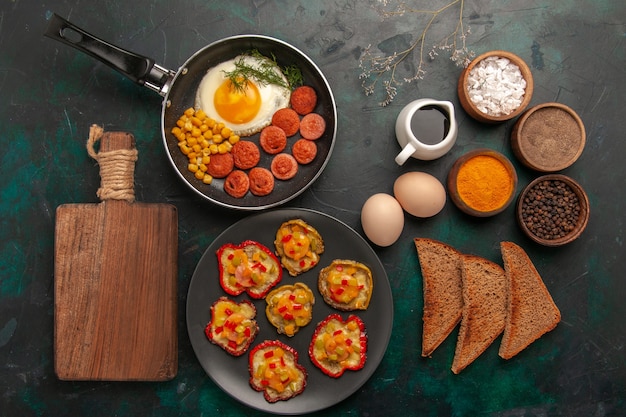 Top view cooked bell-peppers with scrambled eggs bread loafs and sausages on dark-green surface