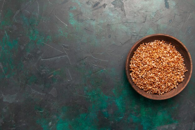 Top view cooked buckwheat tasty meal inside brown plate on dark green surface