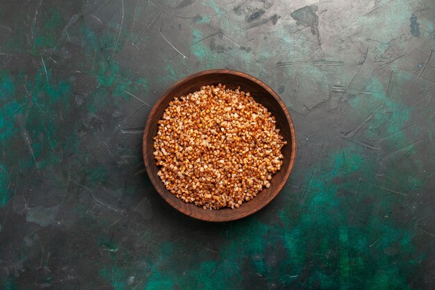 Top view cooked buckwheat tasty meal inside brown plate on dark green surface