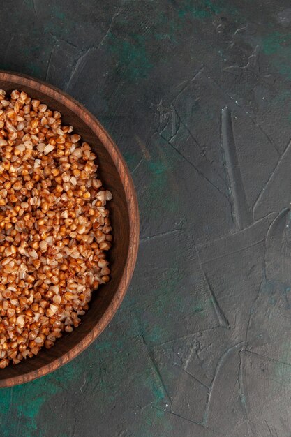 Top view cooked buckwheat tasty meal inside brown plate on the dark green surface