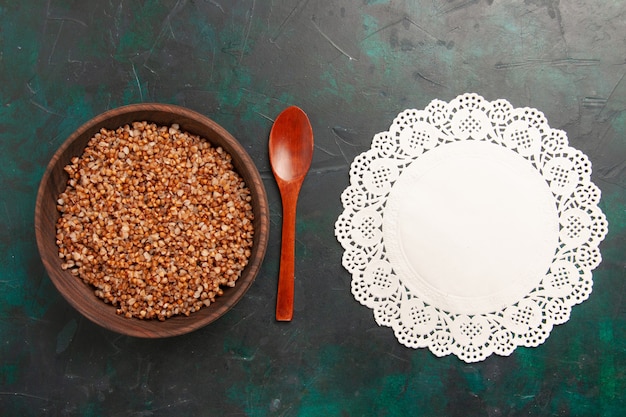 Foto gratuita vista dall'alto cucinato pasto gustoso di grano saraceno all'interno del piatto di legno marrone sulla superficie verde scuro