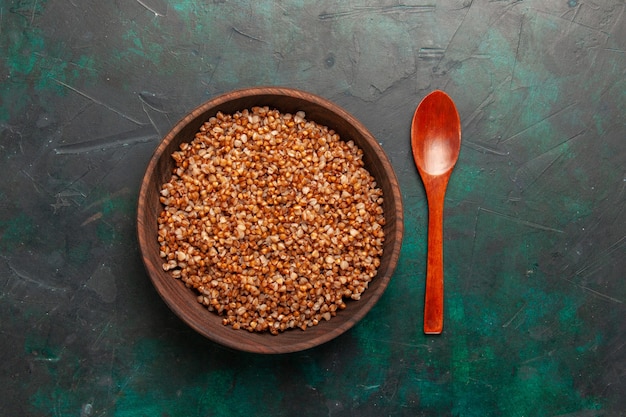 Top view cooked buckwheat tasty meal inside brown wooden plate on the dark green surface