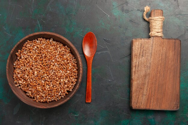 Top view cooked buckwheat tasty meal inside brown wooden plate on the dark green surface