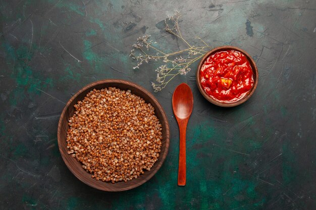 Top view cooked buckwheat with tomato sauce on the dark green surface