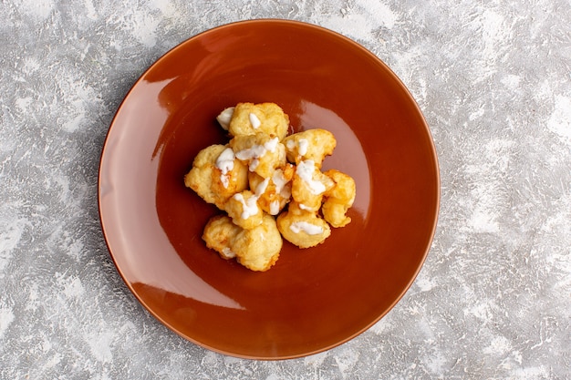 Top view of cooked cauliflower inside brown plate on light surface