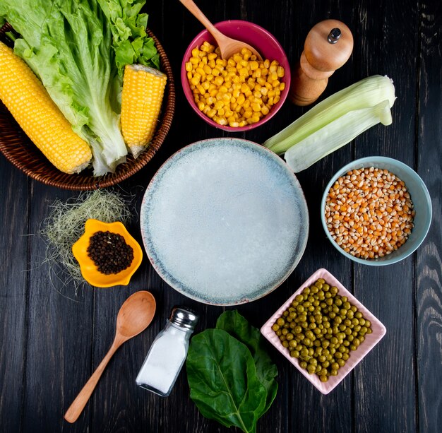 Top view of cooked corns corn seeds empty plate lettuce with corn shell and silk black pepper green peas salt spoon spinach on black