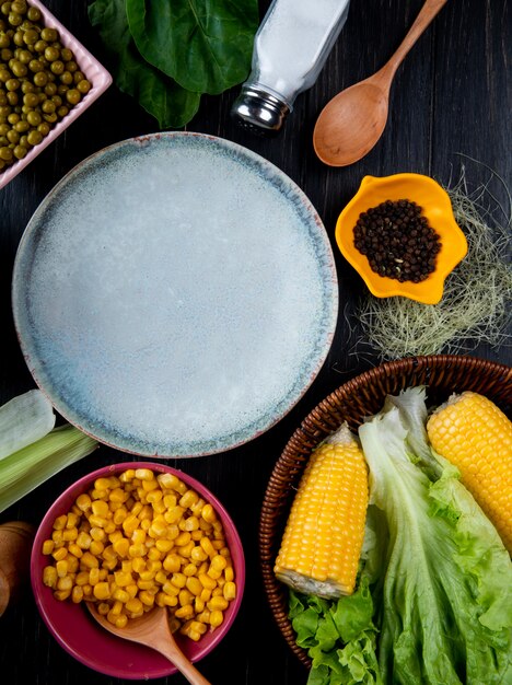 Top view of cooked corns corn seeds empty plate lettuce with corn silk salt spoon spinach on black surface