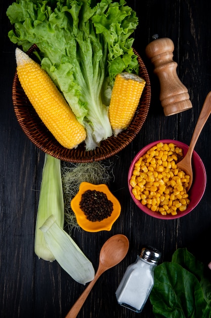 Top view of cooked corns corn seeds lettuce with corn shell and silk salt spoon spinach on black