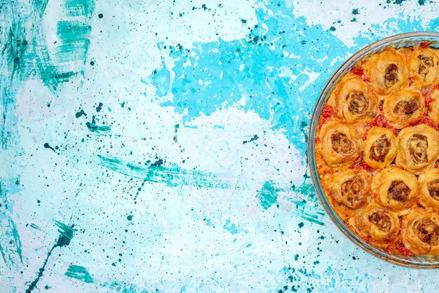Top view of cooked dough meal with minced meat and tomato sauce inside glass pan on bright-blue, cooking bake food meat dough