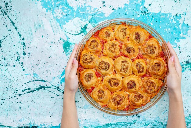 Top view of cooked dough meal with minced meat and tomato sauce inside glass pan on bright-blue desk, bake food meat dough