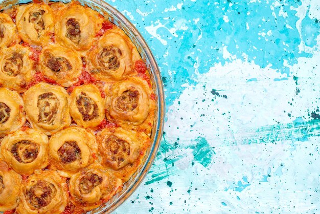 Top view of cooked dough meal with minced meat and tomato sauce inside glass pan on bright-blue desk, cooking bake food meat dough