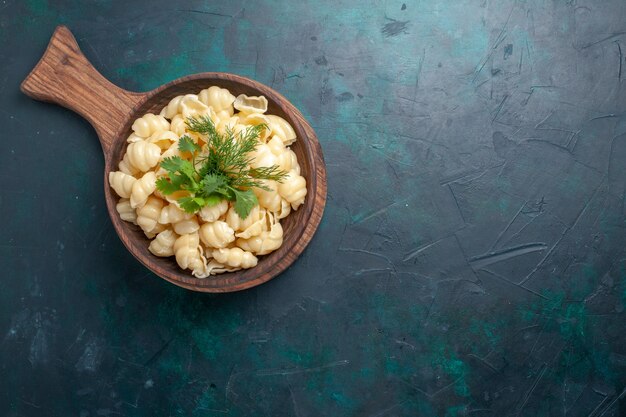 Top view cooked dough pasta with greens inside plate on the dark surface