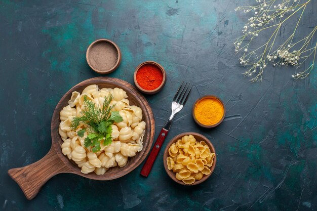 Top view cooked dough pasta with greens and seasonings on dark surface