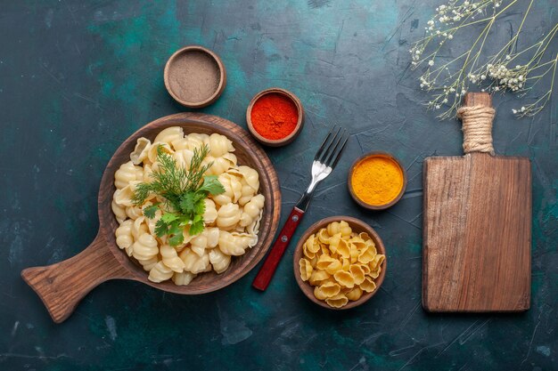 Top view cooked dough pasta with greens and seasonings on the dark surface