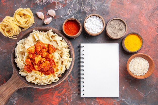 Vista dall'alto pasta cotta con pollo e salsa su un piatto di pasta scura di superficie scura