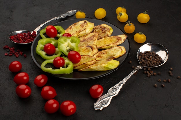 top view cooked eggplant along with sliced green bell pepper and whole red cherry tomatoes inside black plate on the dark floor