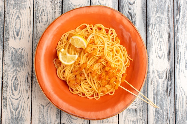 Top view of cooked italian pasta tasty with lemon slices and shrimps inside orange plate on the grey wooden rustic surface