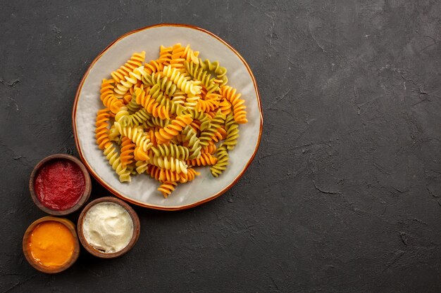 Top view cooked italian pasta unusual spiral pasta with seasonings on dark space