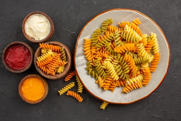 Top view cooked italian pasta unusual spiral pasta with seasonings on dark space