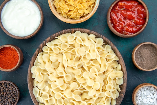 Vista dall'alto di pasta italiana cotta con diversi condimenti sulla scrivania scura