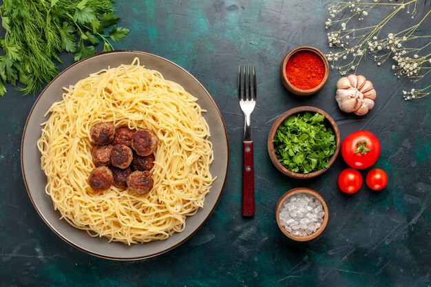 Top view cooked italian pasta with meat balls and greens on dark-blue surface