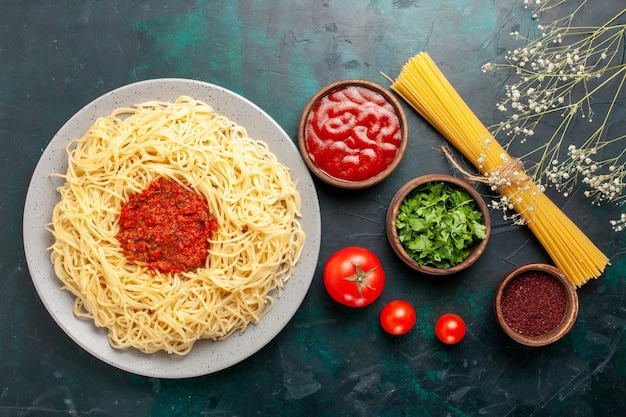 Вид сверху приготовленные итальянские макароны с томатным соусом из фарша и приправами на темно-синей поверхности