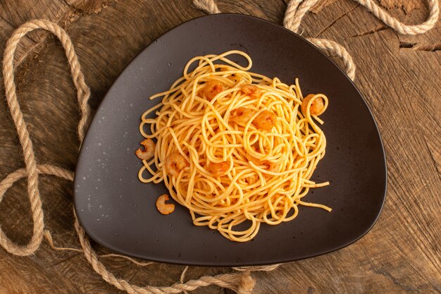 Top view of cooked italian pasta with shrimps inside brown plate with ropes on the wooden desk